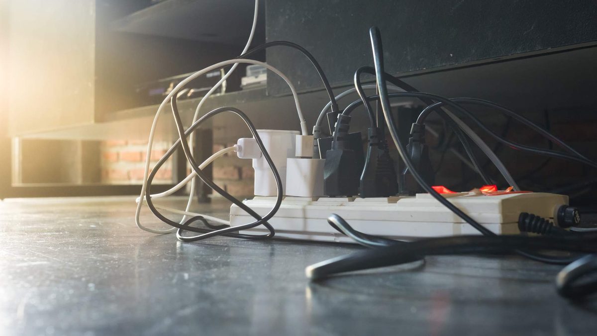 Several plugs and tangled cords crowded into power boards on a floor