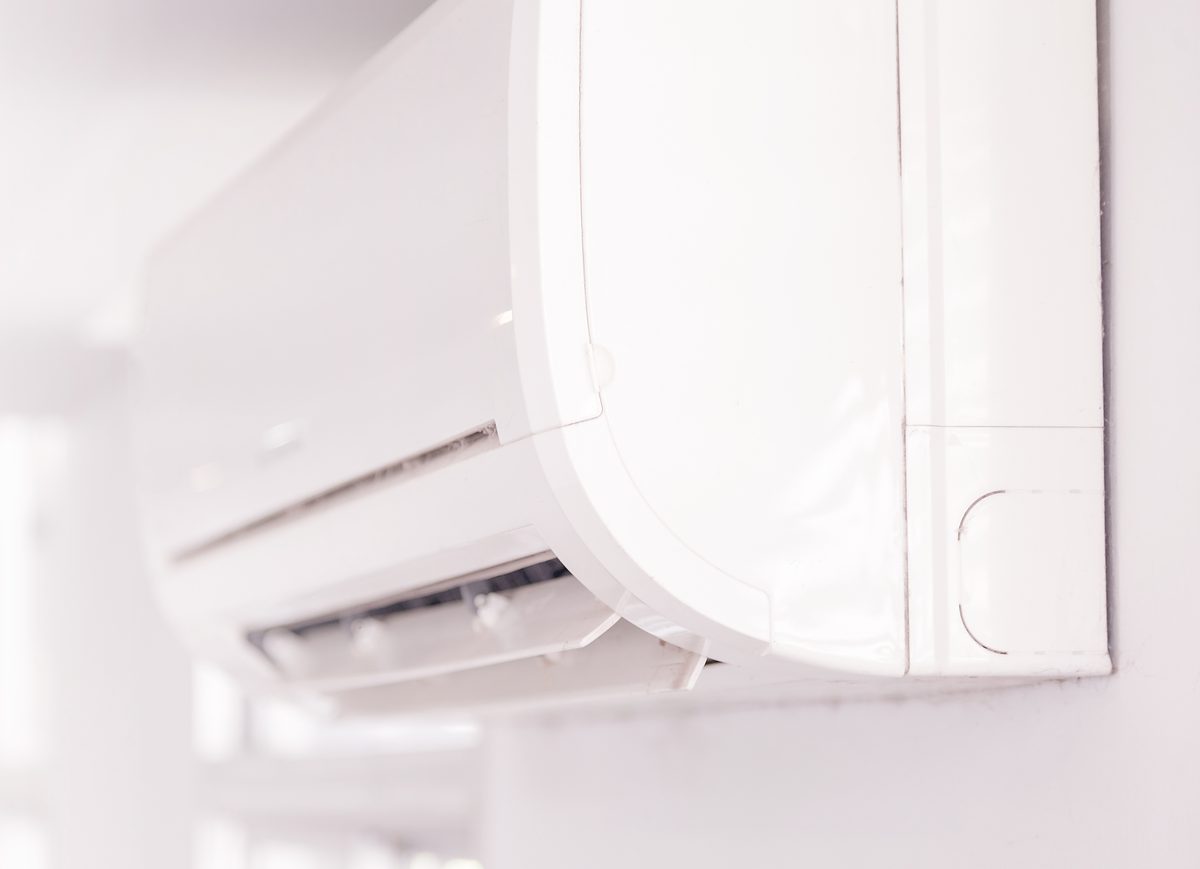 A white wall-mounted heat pump unit high on a wall in a bright room
